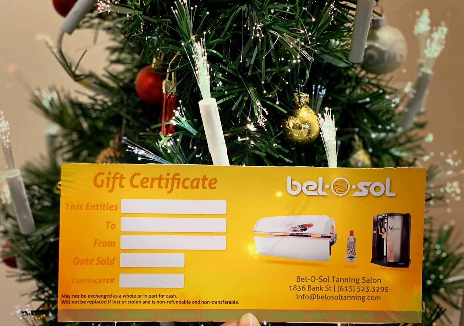 Christmas-themed tanning salon gift certificate near festive tree.